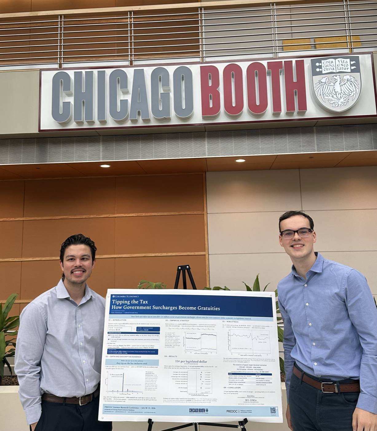 Tyler Sotomayor and Gabriel Uceda-Sosa beside the Tipping the Tax poster under the Chicago Booth sign